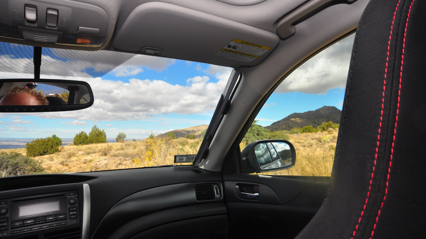 View from inside a car showing dashboard, side mirror, and scenic mountain landscape outside, with a sun shade retractor in place.
